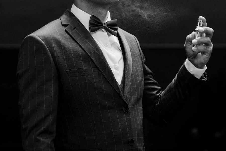 Man in stylish checkered suit, bow tie, spray perfume, dark background