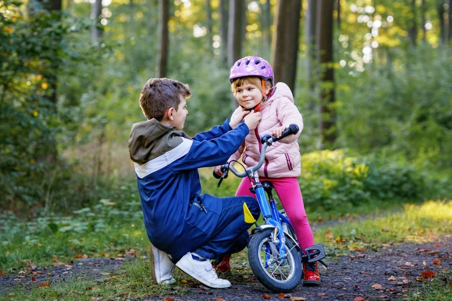 a boy puts on a helmet for a little girl