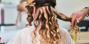 A hairstylist installing hair extensions on a woman
