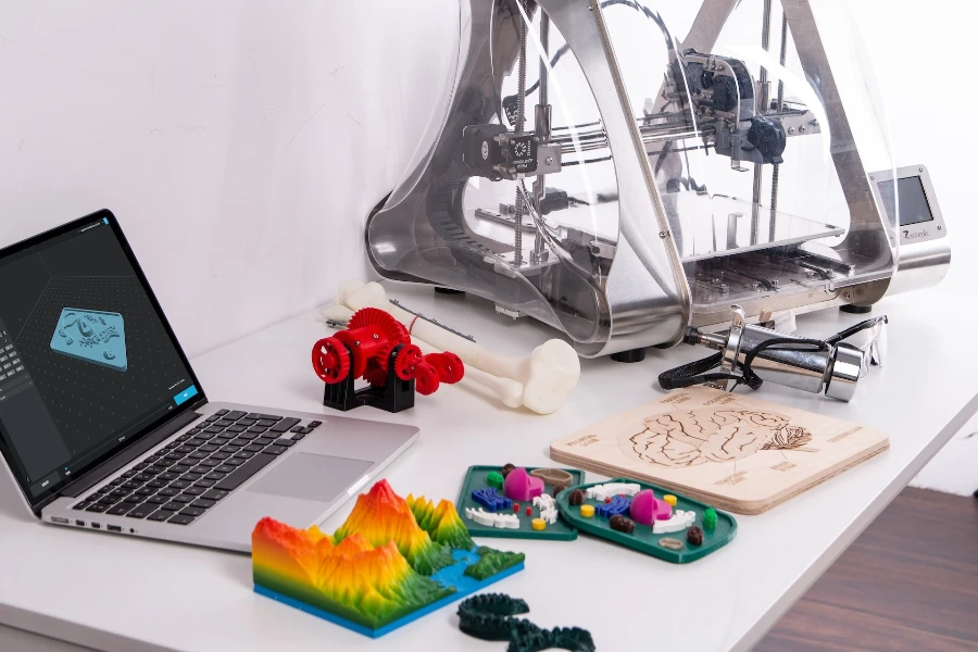 A laptop next to a 3D printer with 3D models