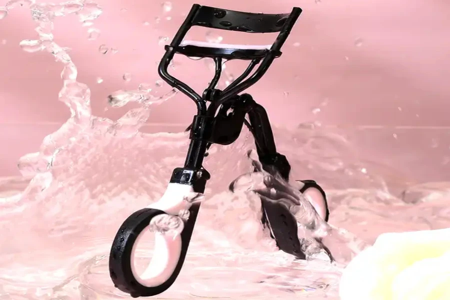 An eyelash curler on watery, pink background