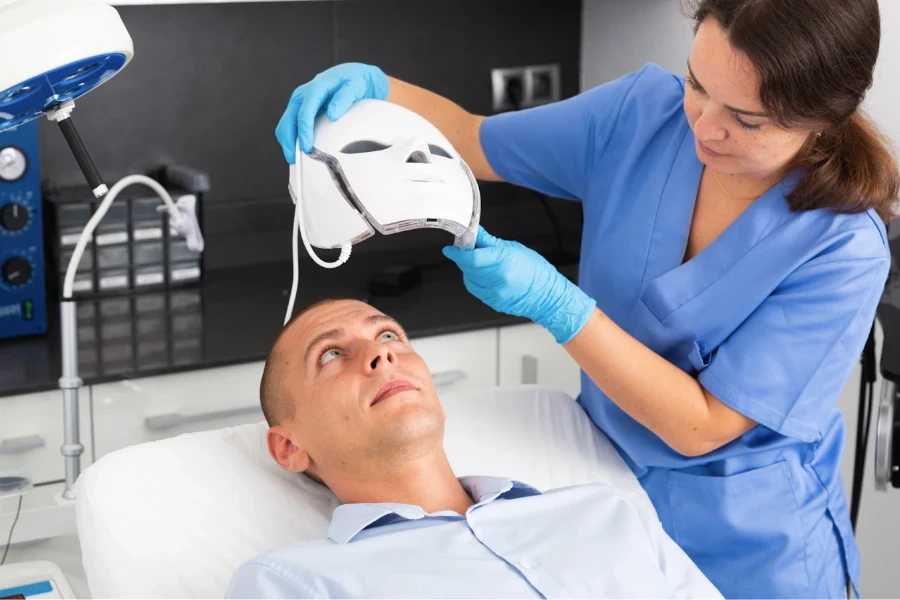 Profesional de la belleza colocando una máscara facial LED a un hombre