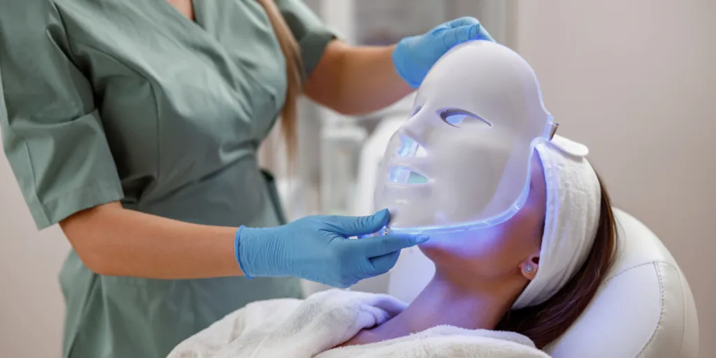 Beauty professional placing LED facial mask on a client’s face