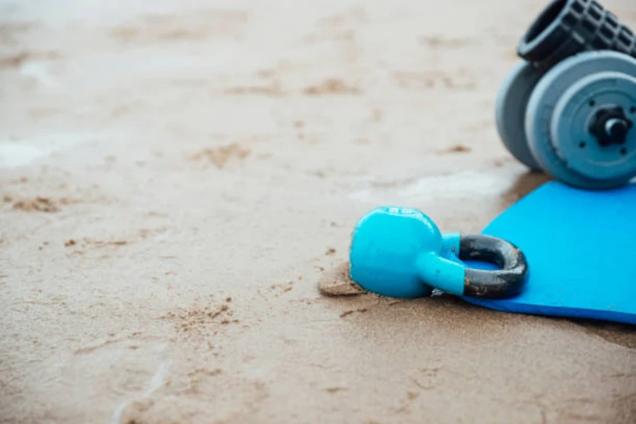 Blue kettlebell sitting next to blue mat on sandy beach