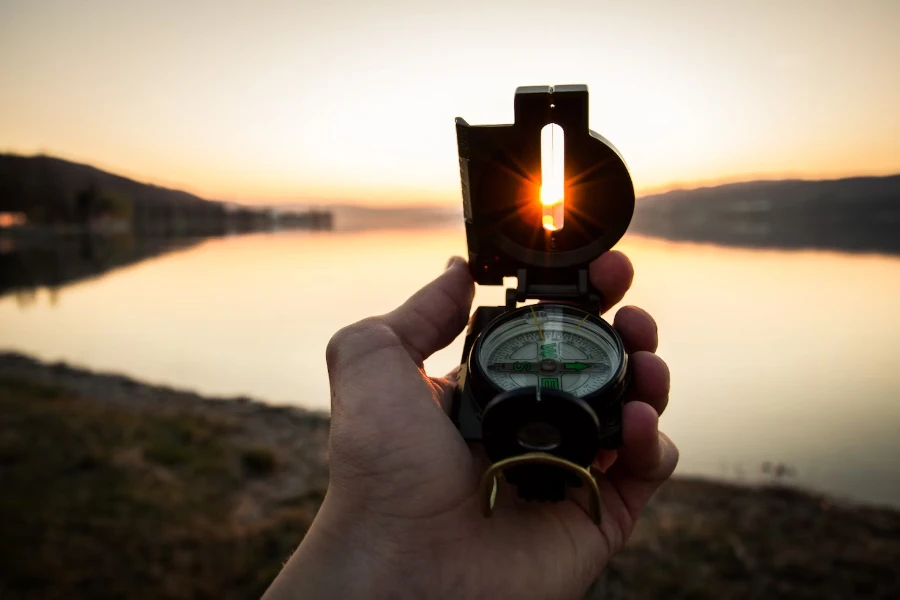 Man holding lensatic compass at sunset next to small lake