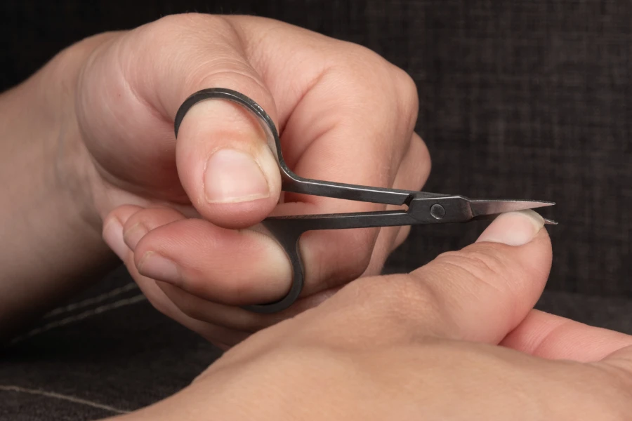 Person schneidet Nägel mit einer Maniküreschere