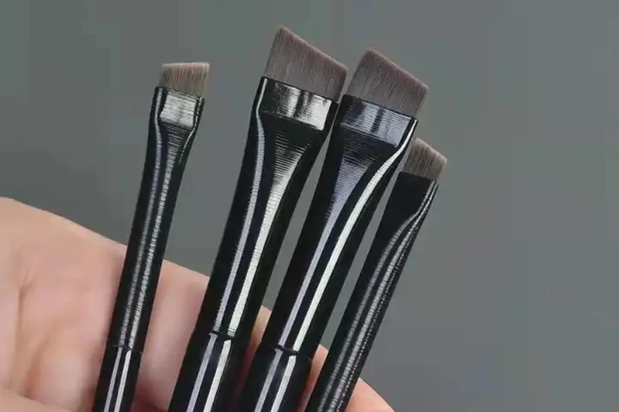 Person holding four eyeliner brushes