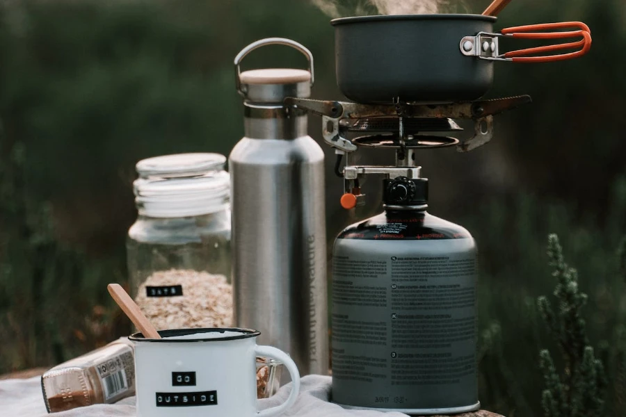 Pot on a portable camp stove beside a water bottle and supplies needed to make oatmeal