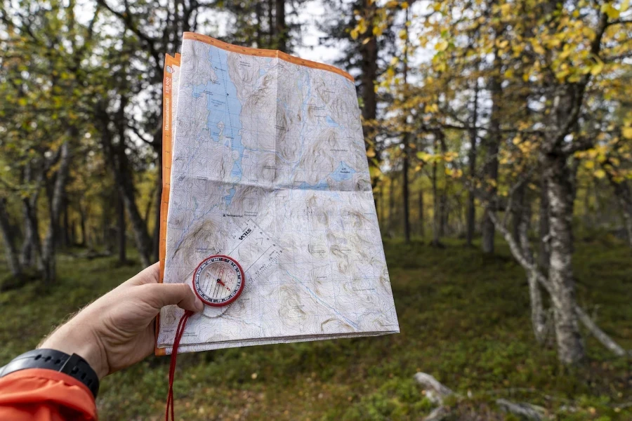 Pequeña brújula magnética sostenida contra un mapa plegado en el bosque