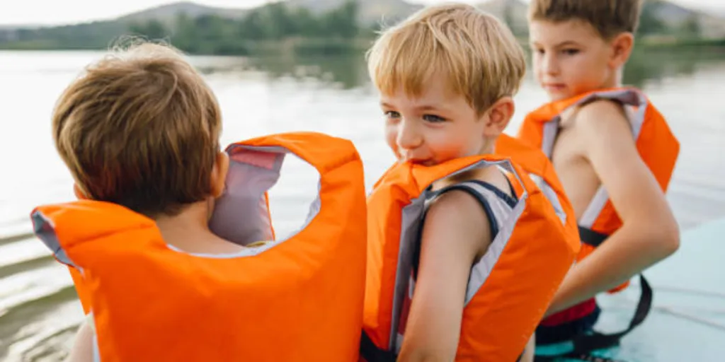 Three kids wearing bright orange life jackets on paddle board