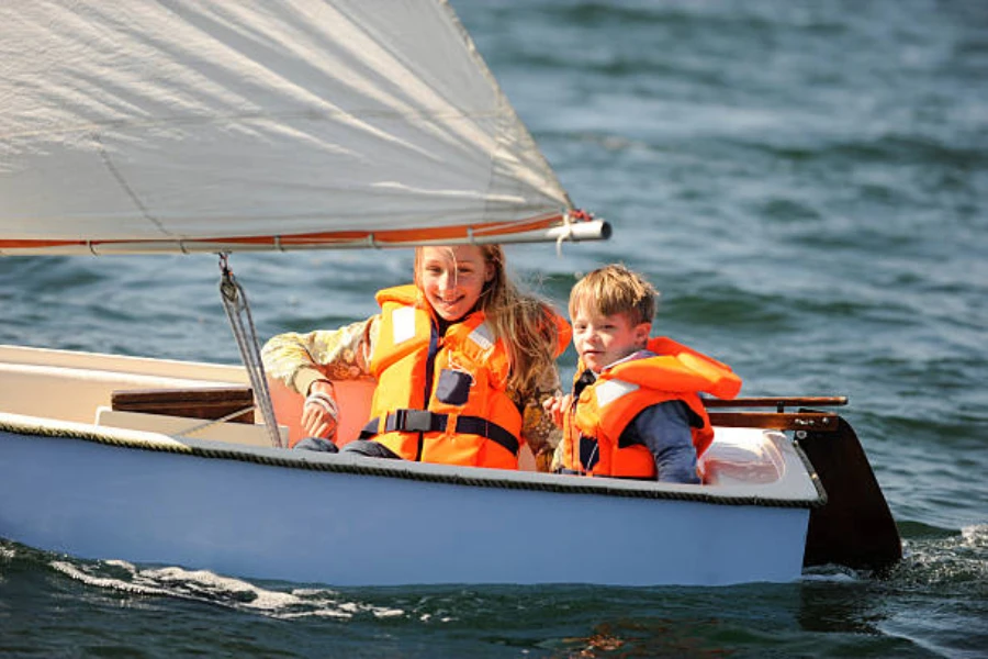 Two kids wearing orange life jackets on small boat
