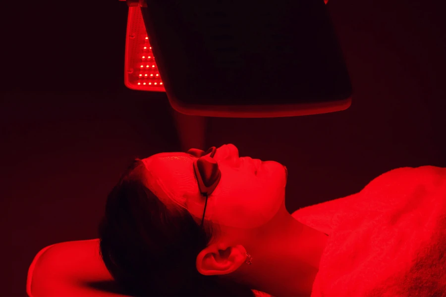 Frau bedeckt ihre Augen auf einem Rotlichttherapiebett