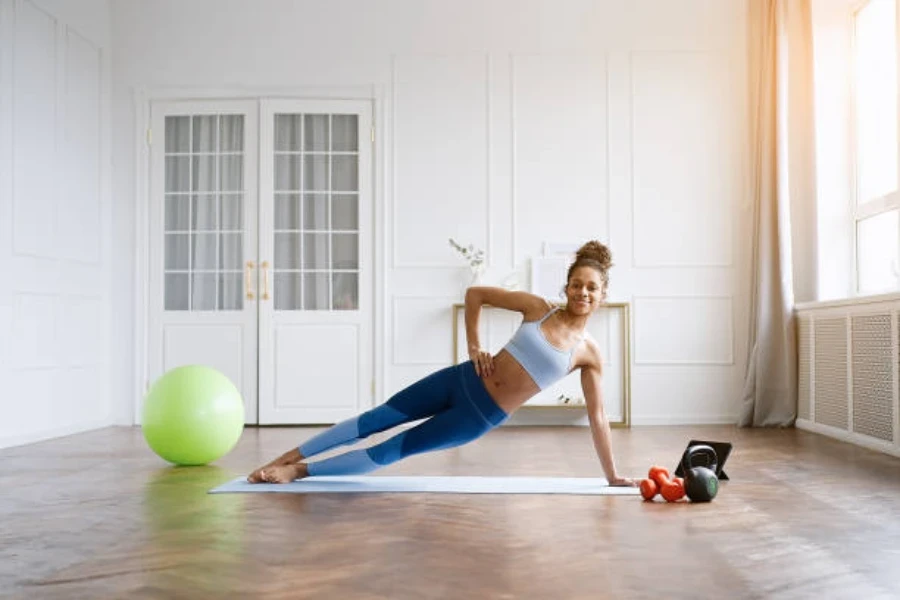 Mujer sosteniendo una tabla lateral sobre una estera de pilates en una habitación grande