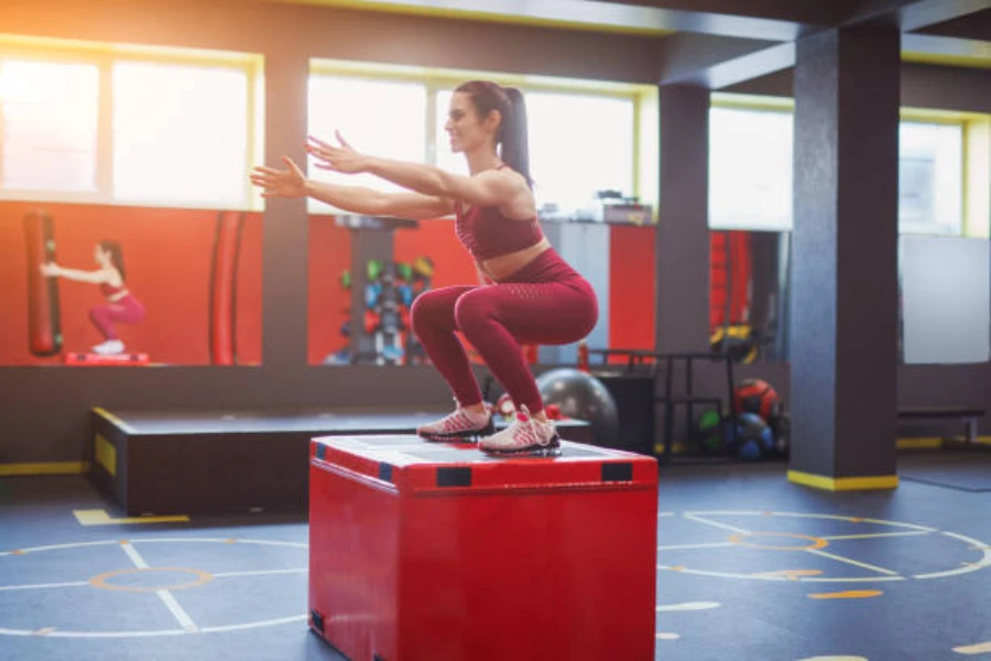 Spor salonunda kırmızı köpük plyo kutusunun üzerine atlayan kadın