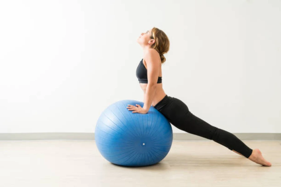 Mujer estirando abdominales usando una gran pelota de pilates azul