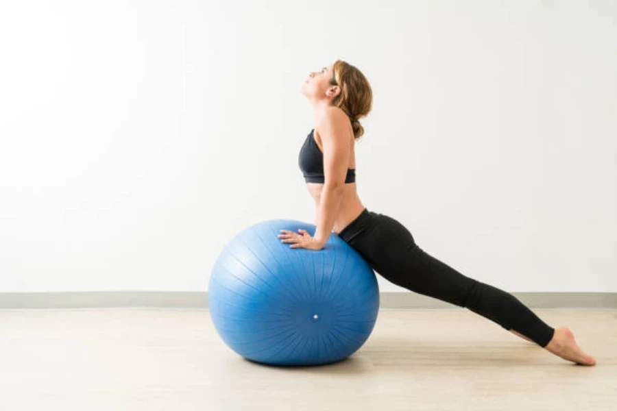 Donna che allunga gli addominali usando una grande palla blu da pilates