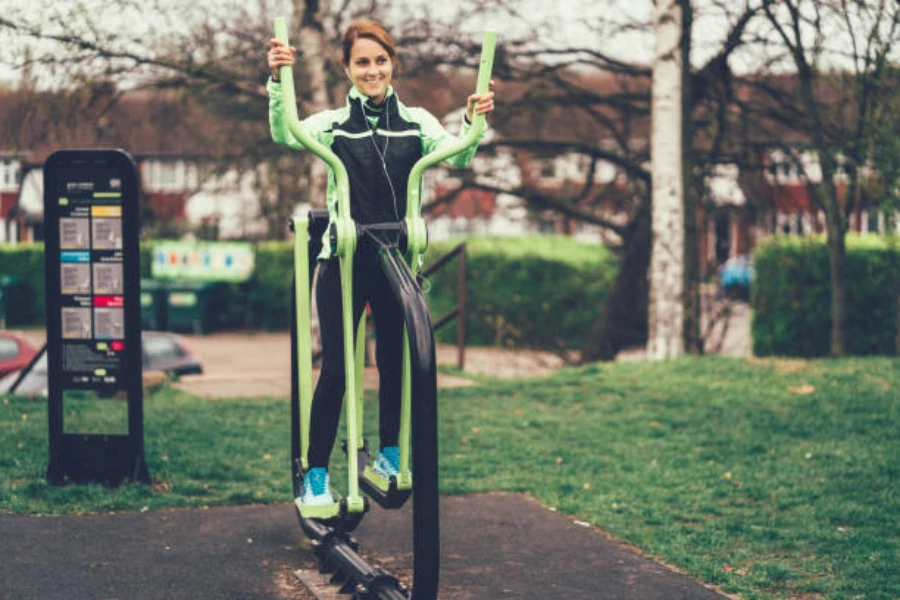 Frau benutzt grünen und schwarzen Outdoor-Ellipsentrainer im Park