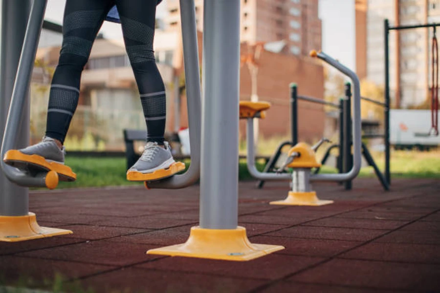Woman using piece of outdoor fitness equipment on padded ground