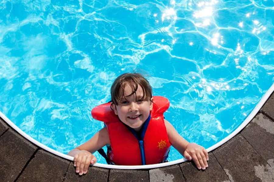 Young boy at edge of pool with orange life jacket