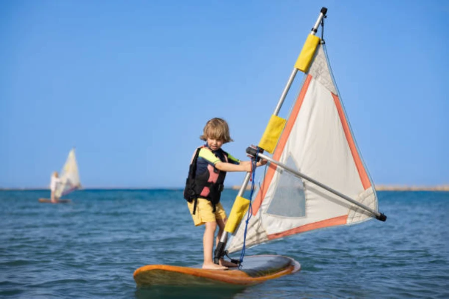 Özel can yeleği giyerken rüzgar sörfü yapan genç çocuk