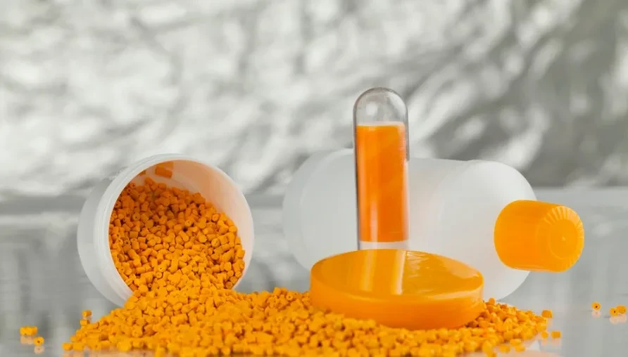 Bright orange masterbatch pellets spilled from an overturned plastic bottle with a matching orange cap