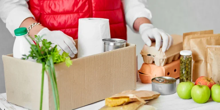 Delivery man employee in red vest packing box with food