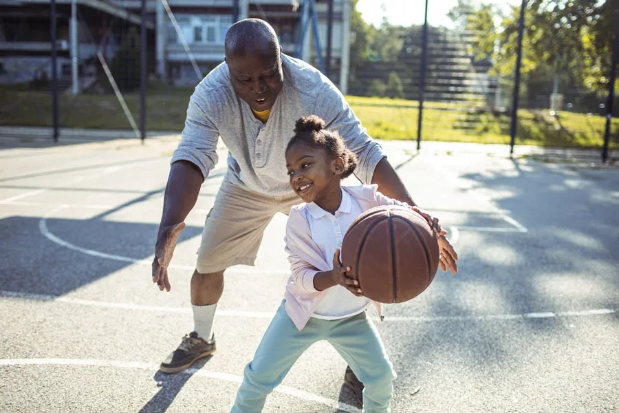 Father playing basketball with young daughter during outdoor play