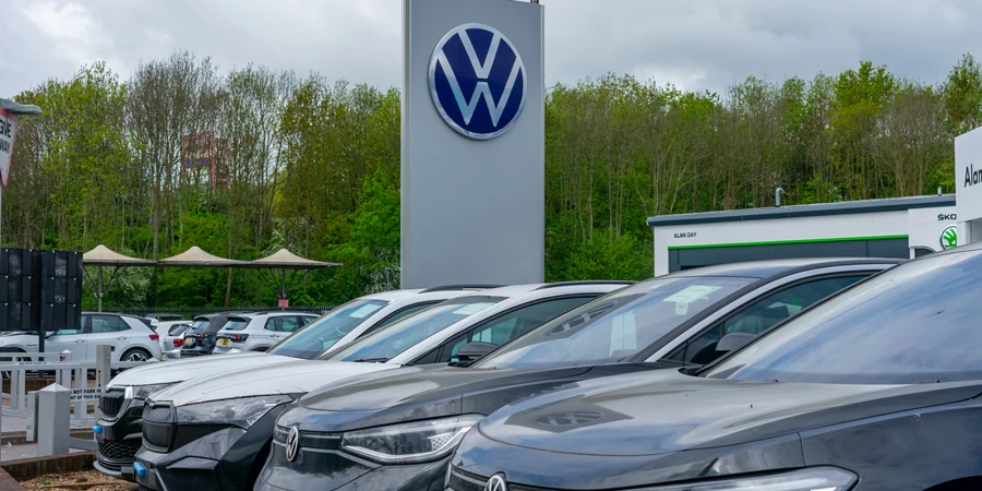 The Volkswagen name sign on the forecourt of a VW car dealer with a display of cars for sale