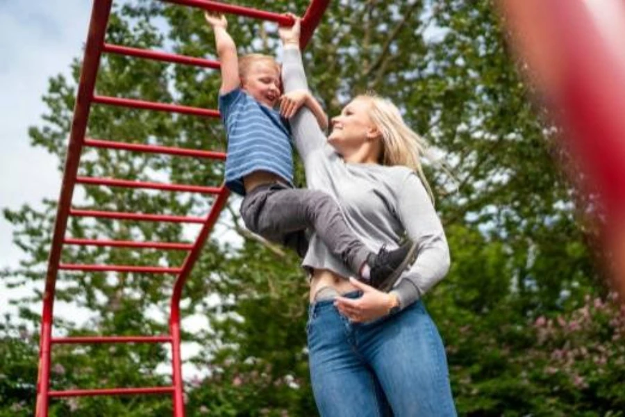 A mother supporting her son through a monkey bar course
