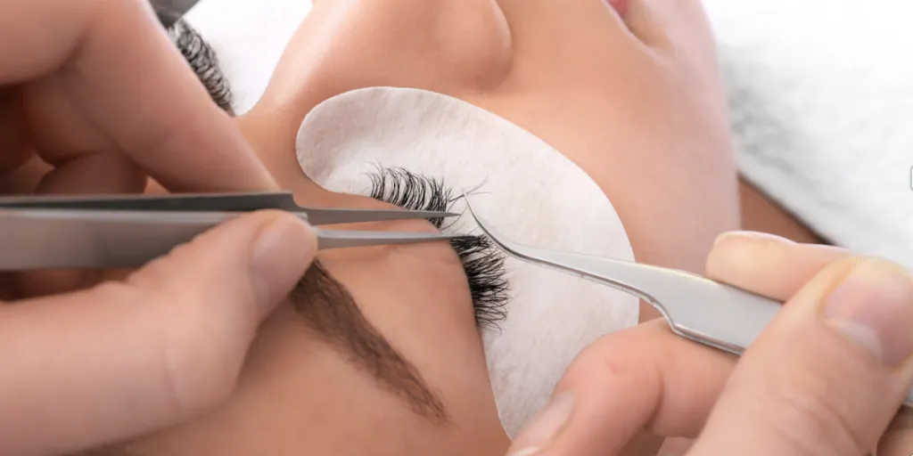 An aesthetician fixing a client's lashes with tweezers