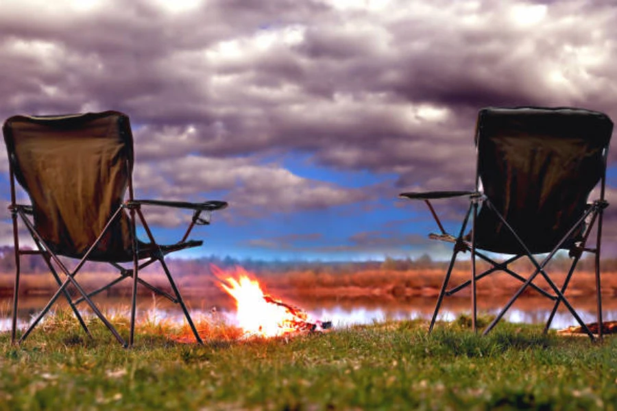Black folding camping chairs sitting next to fire