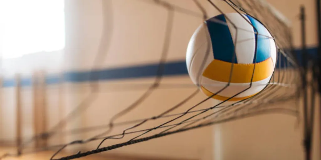Blue, white, and yellow volleyball hit into volleyball net