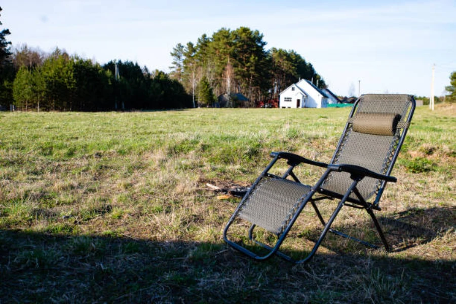 Cadeira de acampamento reclinável marrom sentada em um campo gramado