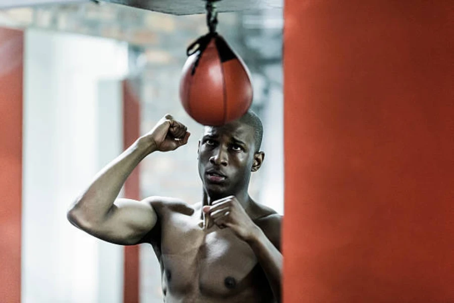 Homme dans une salle de sport frappant un sac de vitesse rouge sans chemise