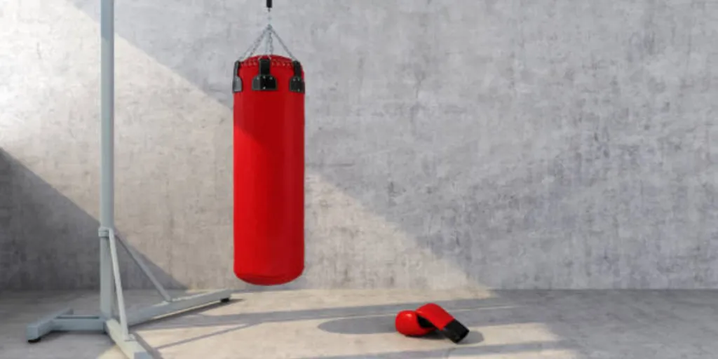 Red punching bag hanging from stand next to boxing gloves