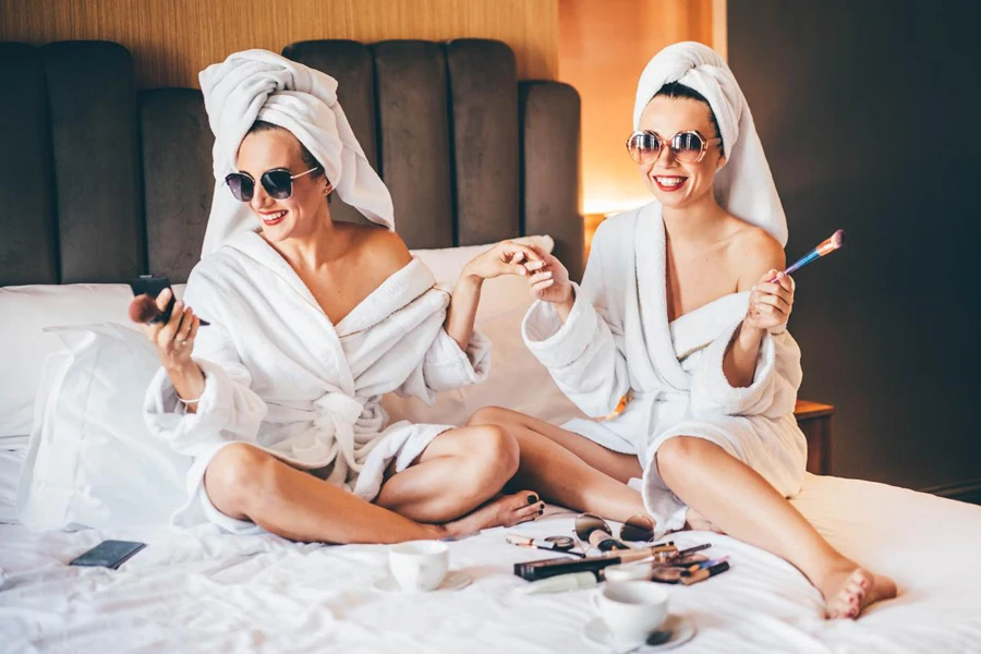 duas mulheres vestindo roupões de banho e aplicando maquiagem