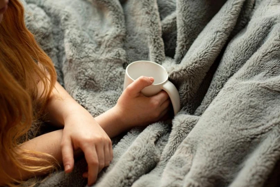 Gri şerpa battaniyenin üzerinde kahve kupası tutan kadın