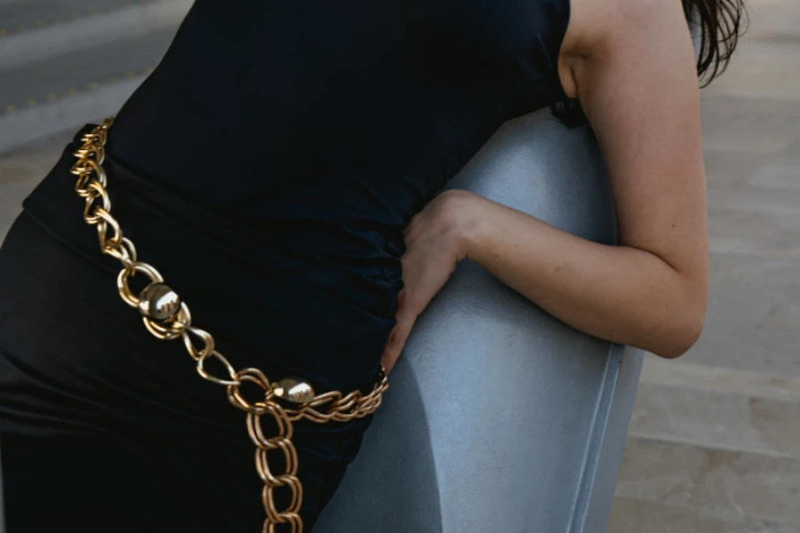 Frau im schwarzen Kleid mit goldenem, klobigem Kettengürtel