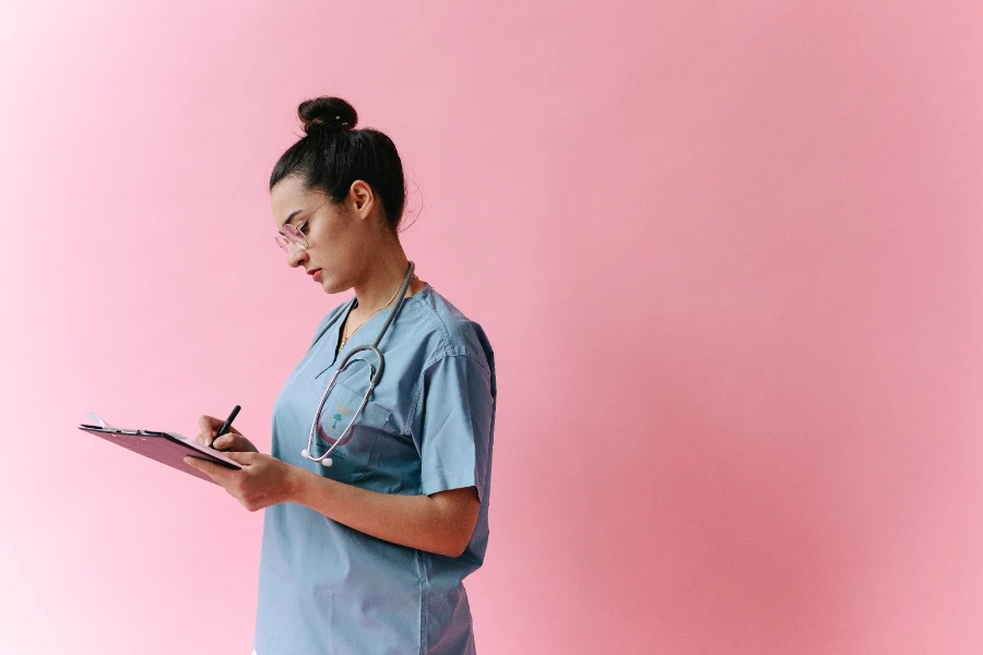 Woman in medical scrubs writing on a clipboard