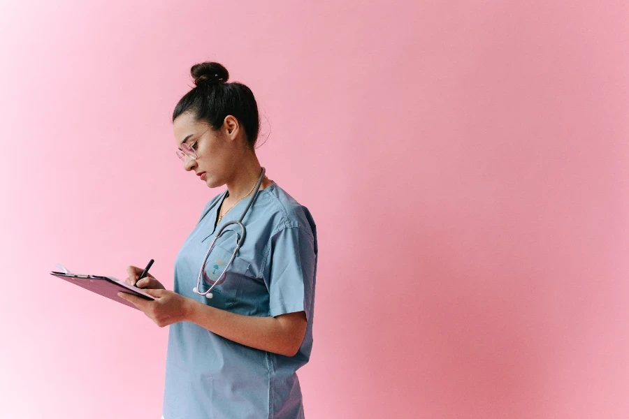 Mulher de uniforme médico escrevendo em uma prancheta