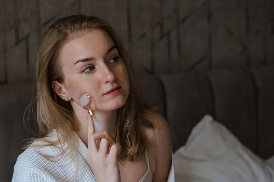 Femme en blanc utilisant des rouleaux de glace sur son visage