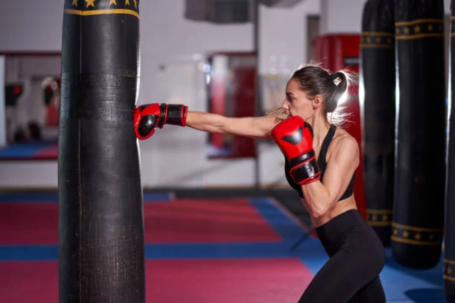 Femme frappant un sac lourd noir avec des gants de boxe rouges