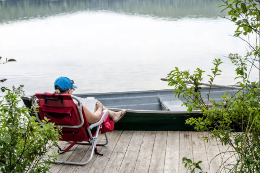 Göl kenarında kırmızı sallanan kamp sandalyesinde oturan kadın