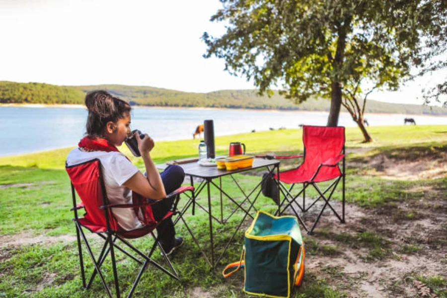 Frau sitzt im roten Campingstuhl mit aufgestelltem Tisch