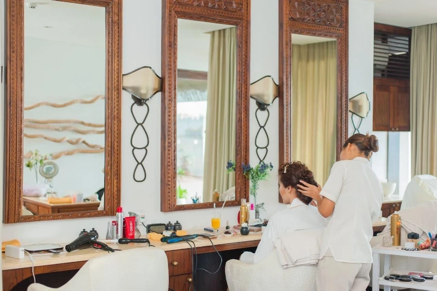 Woman tending to a client sitting in front of a mirror