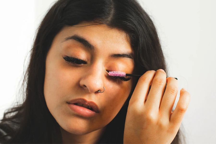 Jeune femme utilisant un mascara avec une brosse rose