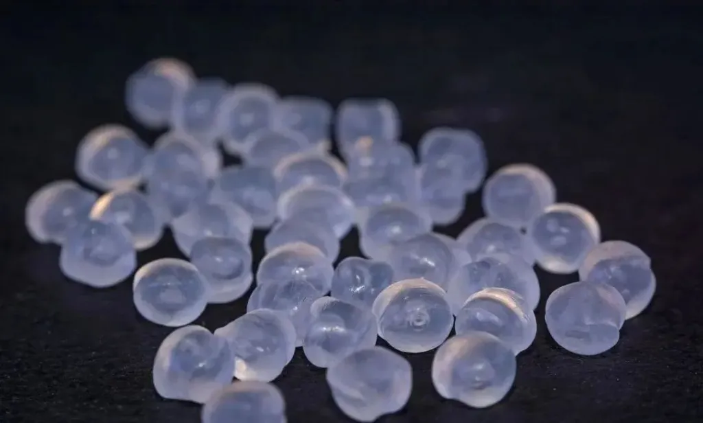 A collection of translucent, round polypropylene pellets scattered on a dark surface