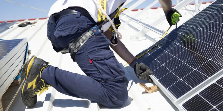 Seorang pekerja mengukur panel surya dengan meteran untuk memasangnya di atap