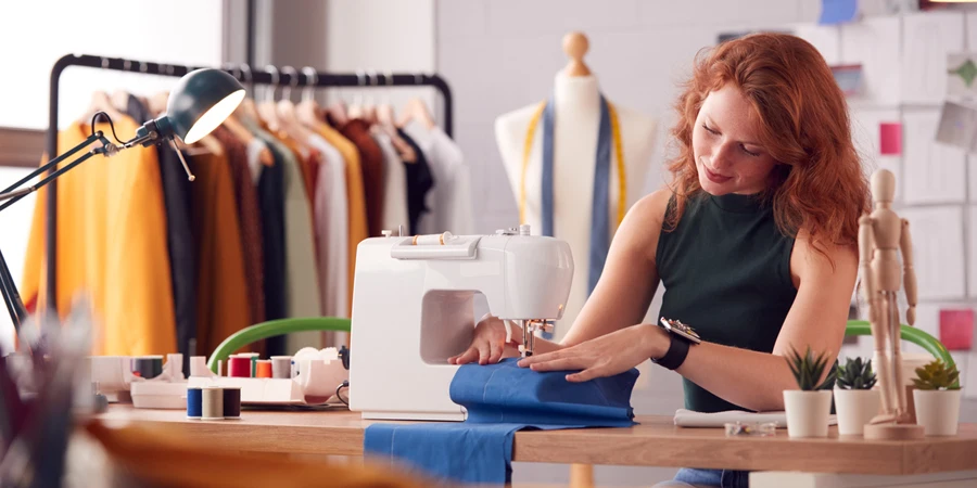 طالبة أو صاحبة عمل تعمل في مجال الأزياء باستخدام ماكينة الخياطة في الاستوديو