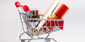 Front view of a shopping cart with makeup products on a pink background